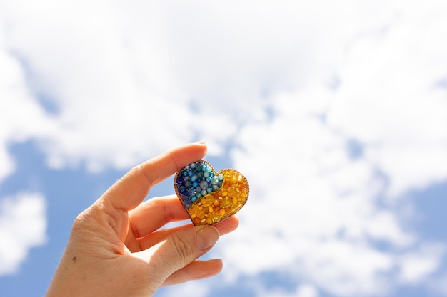 broche in de vorm van een hart in geelblauwe kleur tegen de luchtkleuren van de vlag van Oekraïne