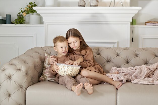 Broer en zus eten popcorn om thuis op de bank te zitten