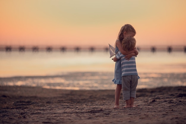 Broer en zus houden van elkaar kleine jongen en meisje knuffels aan de kust op reis prachtige zonsondergang Reizen met kinderen dromen vakantie vriendelijke familie en vrije tijd concept