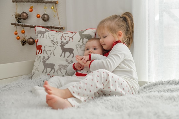 Broer en zus in kerstpyjama zitten op het bed met versieringen.