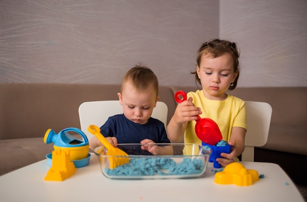 Broer en zus spelen met zand aan de tafel in de kamer. Spelen met kinetisch zand.