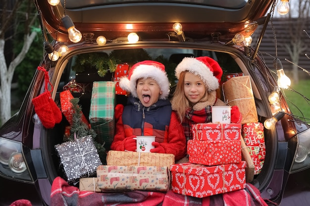 Broer en zus zitten in de auto versierd met oud en nieuw een heleboel geschenkdozen