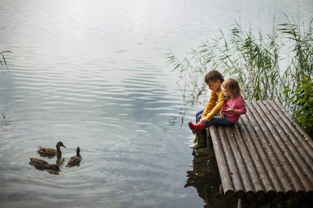 Broer en zus zitten op de rivierpier en knuffelen en kijken naar eenden in het water