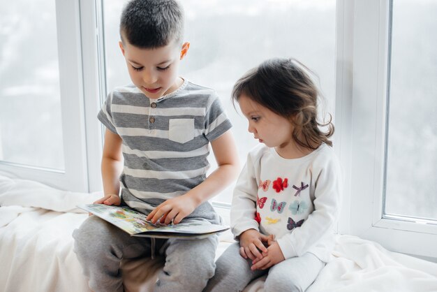 Broer en zus zitten op de vensterbank en lezen een boek. geluk, familie