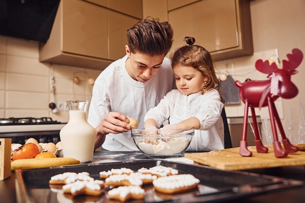 Broer met zijn kleine zusje die voedsel bereidt door bloem in de keuken te gebruiken en plezier te hebben.