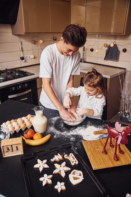 Broer met zijn kleine zusje die voedsel bereidt door bloem in de keuken te gebruiken en plezier te hebben.