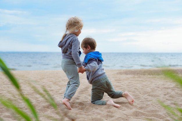 Broers en zusje tijdens zomervakanties plezier op zandstrand meisje helpt jongen op te staan Ondersteuning voor kinderen