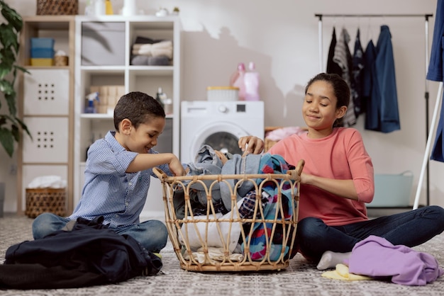 Broers en zussen halen de gewassen kleren uit de rieten mand, ze sorteren de was