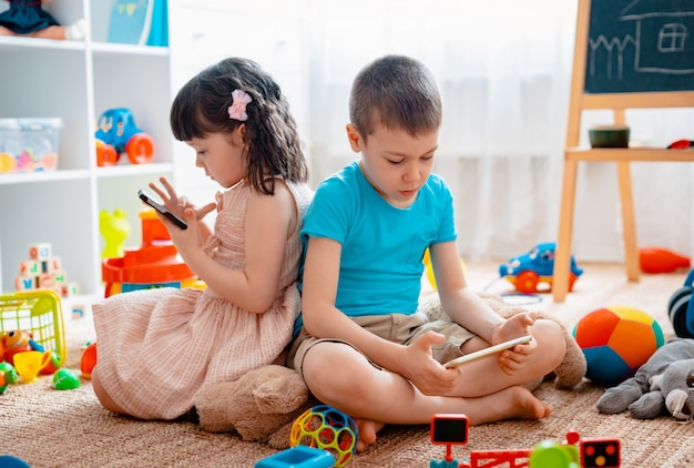 Broers en zussen, kinderen, broer en zus, vrienden zitten op de vloer, speelkamer voor kinderen met smartphones, los van het verspreide speelgoed.