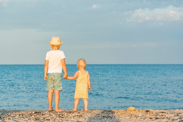 Broers en zussen op het strand. Achteraanzicht. Broer houdt de hand van zusje vast.