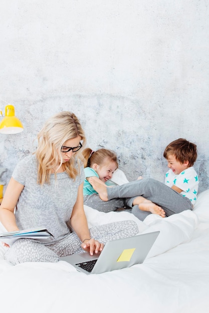 Broers en zussen spelen op het bed terwijl de moeder thuis aan de laptop werkt