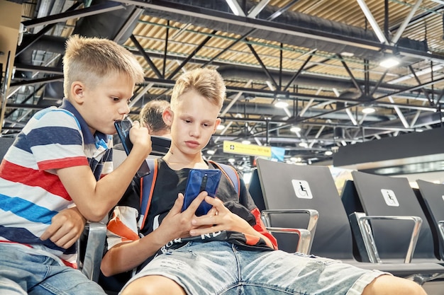 Broers spelen games en delen interesses met behulp van smartphones in de wachtzaal met fauteuils op de luchthaven