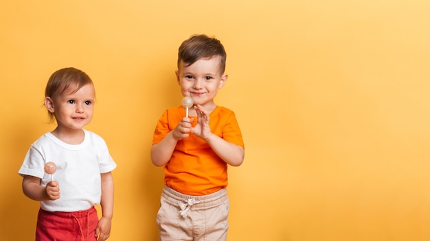 Broertje en zusje eten een zoete lolly op een stokje. Gele achtergrond. Het concept van preventie van cariës en diabetes bij kinderen. Plaats voor uw tekst