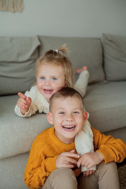 Broertje en zusje in knusse gebreide truien spelen thuis. Portret van schattige kleine broer en zus. Vallen.