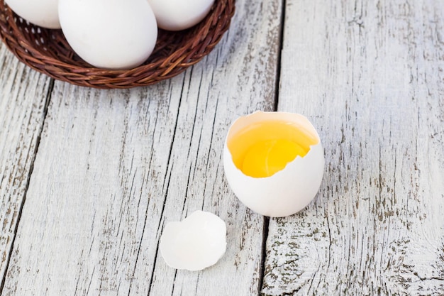 Broke One whole egg amongst white eggs in basket on a white wooden background