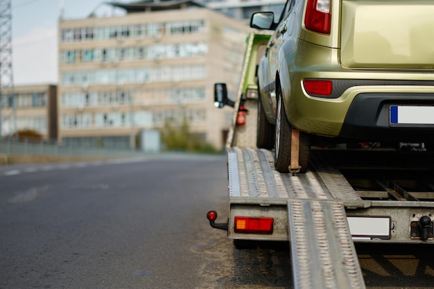 Broken car standing on fixed flatbed tow truck being\
transported for repair. breakdown on road