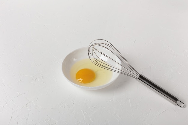 Photo a broken chicken egg in a white plate on a white background. whisk for stirring.