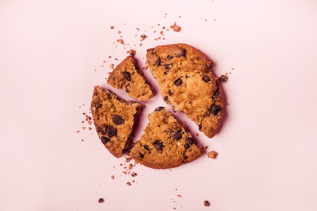 Broken chocolate chip cookie and crumbs on pink background closeup.