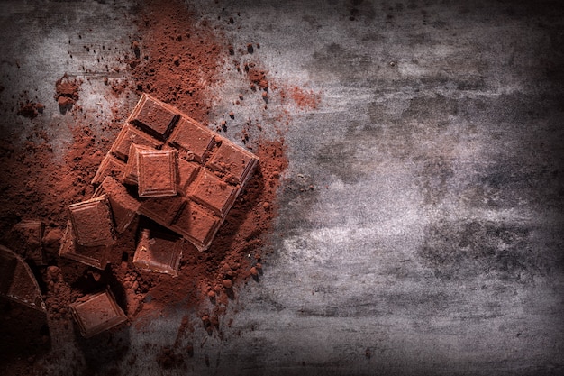 Broken chocolate pieces and cocoa powder on wooden background