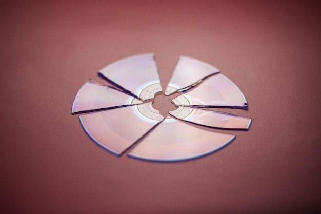 Broken compact disc divided into parts closeup on a redburgundy background complete loss of data