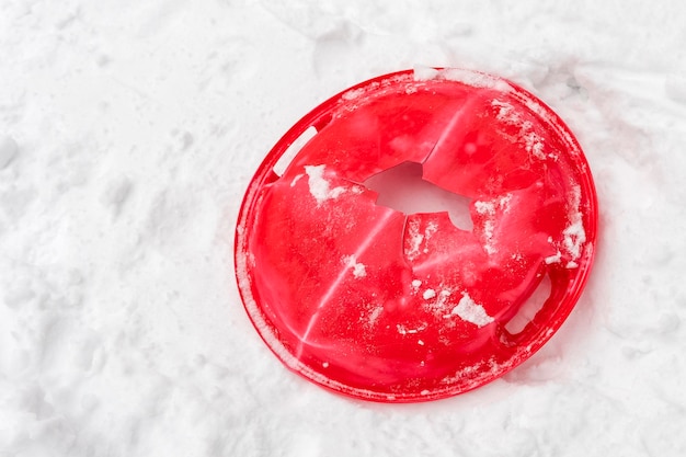 雪の上の壊れたひびの入った赤いプラスチックの受け皿
