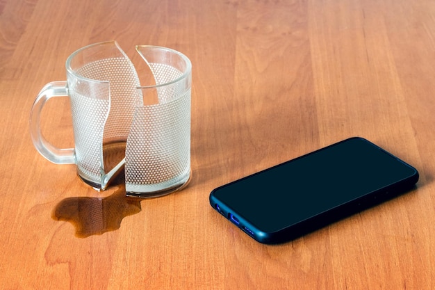 Broken cup and mobile phone smartphone in the office on a wooden table