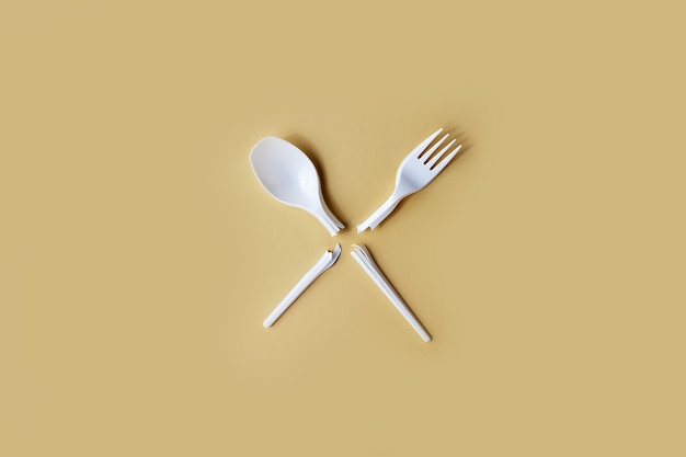 Broken disposable plastic fork and spoon on a uniform background.