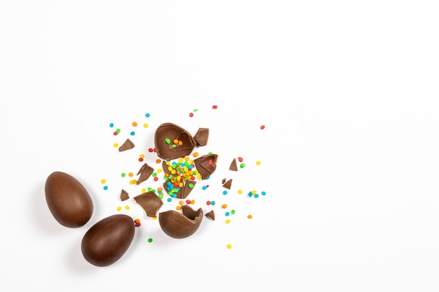 Разбитые пасхальные шоколадные яйца и красочные украшения на светлой поверхности. Пасхальная концепция, пасхальные угощения. Плоская планировка, вид сверху