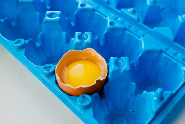 Broken egg in a bright blue container. White abstract background. Egg shell and yelow yolk