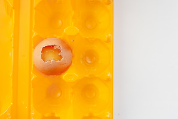Разбитое яйцо в ярко-желтый контейнер. Белый абстрактный фон. Яичная скорлупа и желток