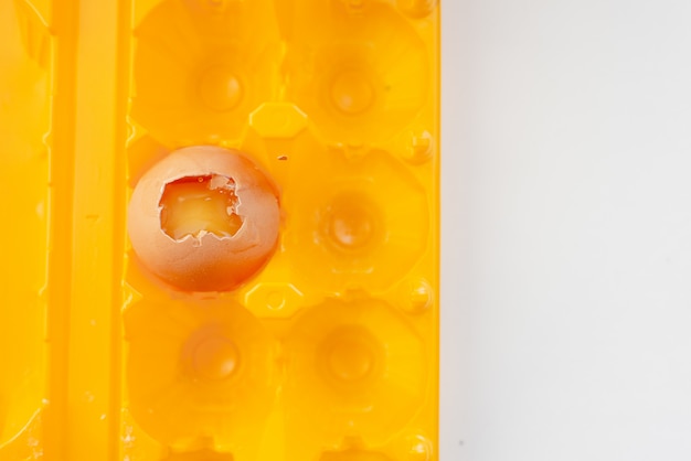 Broken egg in a bright yellow container. White abstract background. Egg shell and yelow yolk