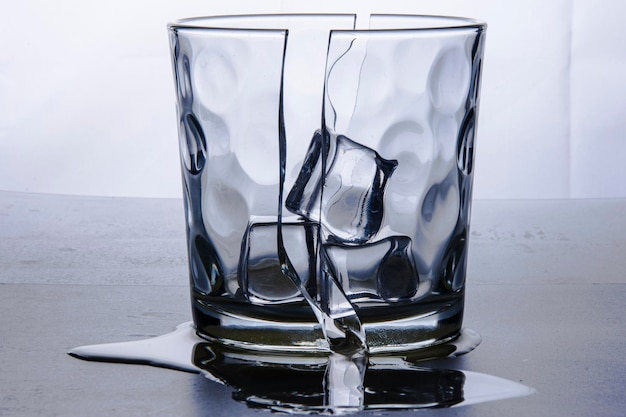 Photo broken glass glass in two halves with an ice cube broken glass glass in two halves with three ice cubes