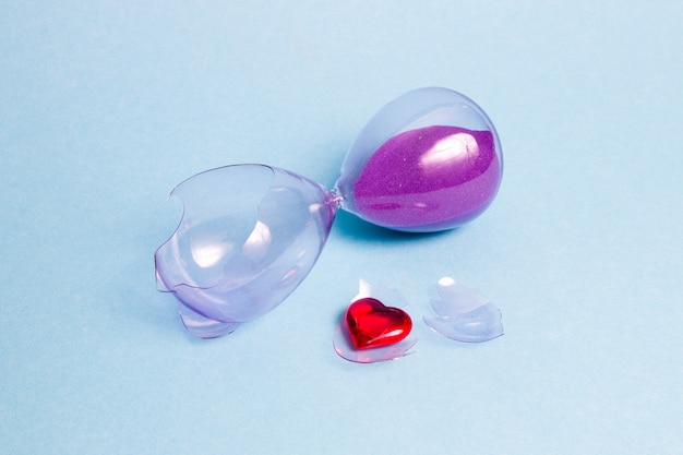 Broken glass hourglass with purple sand on a blue surface