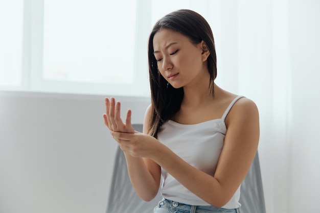 Broken hand cramp upset suffering tanned beautiful young asian\
woman touching massaging painful hand wrist at home interior living\
room injuries poor health illness concept cool offer banner