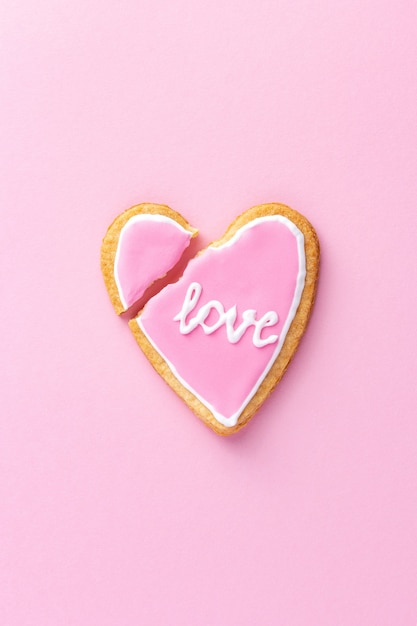 Broken heart shaped cookie with word love on pink as a symbol of the end of the relationship