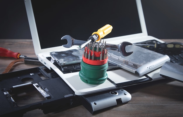 Broken laptop with a wrench and screwdriver on the table. Computer repair service