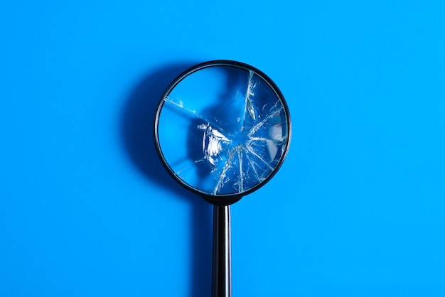 Broken magnifying glass with cracks on blue background top view