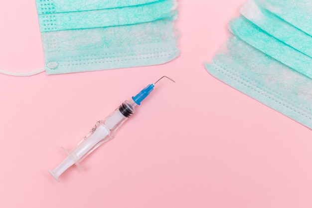 Broken medical syringe and torn medical face mask on the pink background