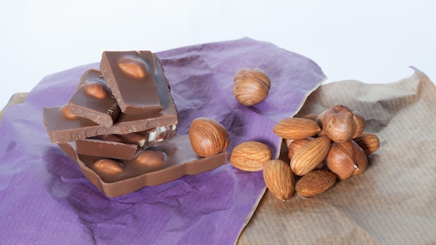 Foto barretta di cioccolato al latte rotto mandorle e nocciole su superficie di carta lilla beige primo piano