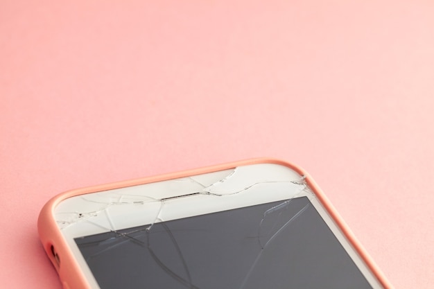 Сломанный телефон с трещиной на стекле дисплея на розовом фоне. Скопируйте место для текста.