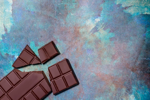 Broken pieces of chocolate on blue abstract background Top view