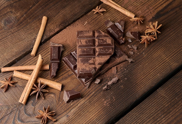 Broken pieces of dark chocolate cinnamon sticks and star anise on a brown wooden table top view