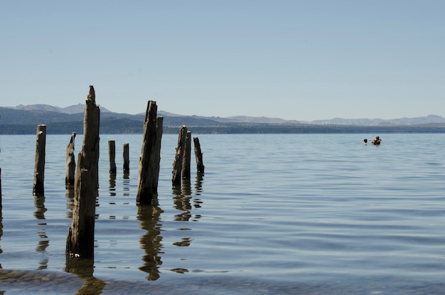 broken pier in lake with boys in water playing and mountains in background