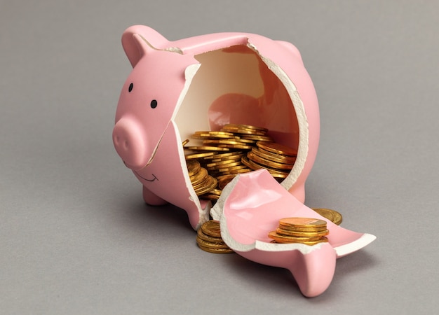 Broken piggy bank with coins inside on gray background.