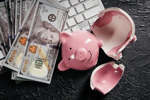 Broken piggy and money on keyboard Concept of cyber crime and online fraud Bankruptcy or lost of savings