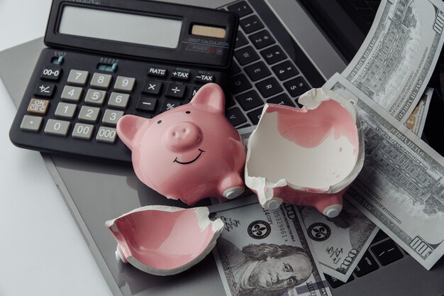 Broken pink piggy bank on a keyboard, calculator and dollar bills