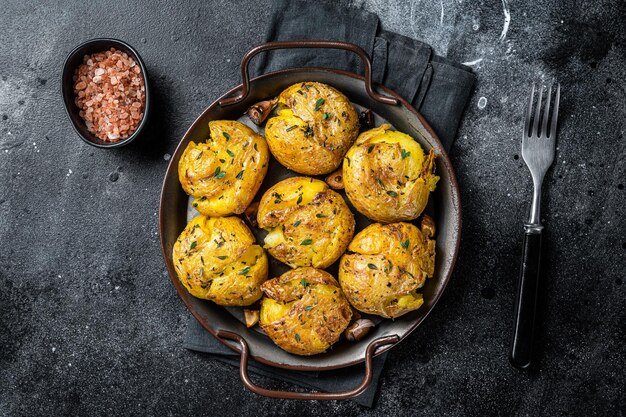 Broken potatoes baked in oil with herbs Black background Top view