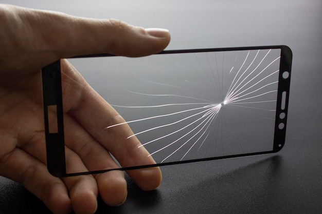 Broken protective glass of smartphone with cracks in hand on black background