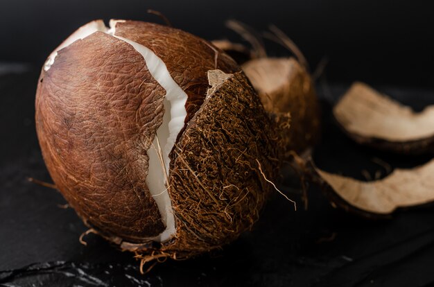 Broken raw coconut on black. Diet and vegetarian food concept.