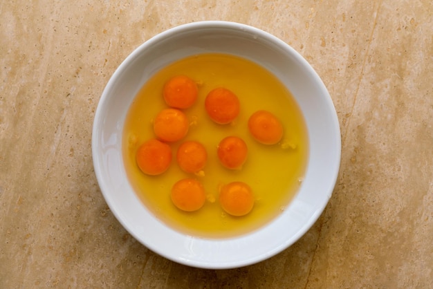 Broken raw eggs in a white plate on a stone surface